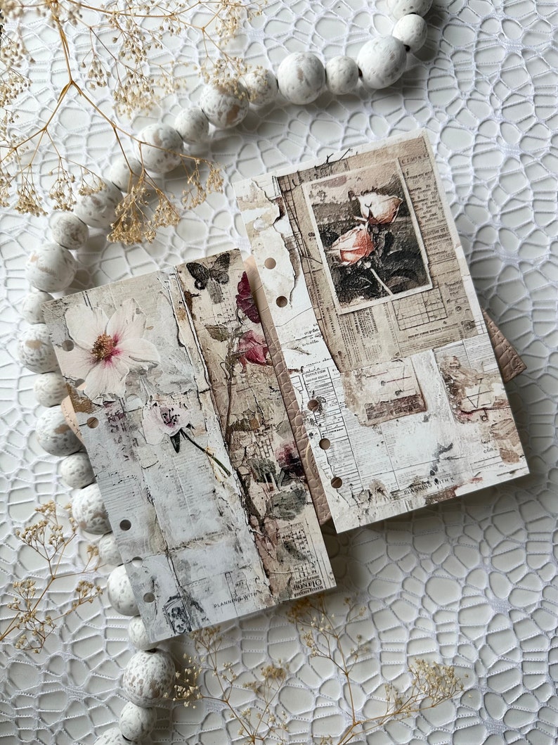 May include: Three white pages with a distressed, vintage look. Each page features a different floral design, including a pink rose, a white flower, and a butterfly. The pages are bound together with metal rings.
