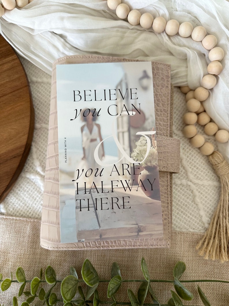 May include: A pink leather planner with a motivational quote that reads "Believe you can & you are halfway there".