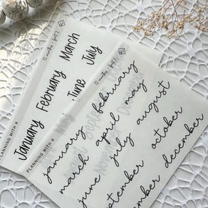 May include: A set of twelve clear stickers with handwritten month names in black ink. The stickers are designed for use in planners and journals.