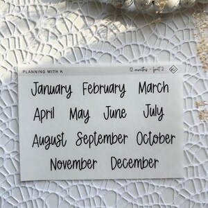May include: A white sheet of paper with black text that reads "PLANNING WITH K" and "12 months - font 2". The sheet contains the months of the year written in a handwritten font.