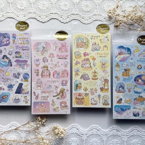 May include: Four rectangular sticker sheets featuring various pastel-colored illustrations of characters, furniture, and celestial objects. Each sheet has a gold circular label at the top and includes printed text such as Endless Space, Dress up smartly, Playful mood, and Midnight.