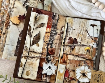 May include: A collection of journals with mixed media art covers. The covers feature collages of dried leaves, flowers, and textured paper in neutral tones. The journals have brown leather-like spines and are open to reveal the inside pages.