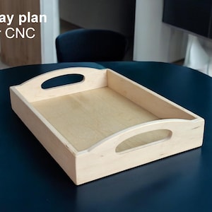 Puede incluir: Una bandeja de madera clara con forma rectangular y asas curvas. La bandeja está sobre una superficie azul oscuro. El texto "Tray plan for CNC" está en la esquina superior izquierda.