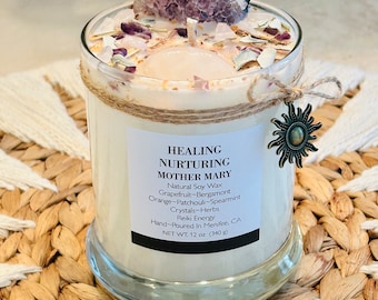 May include: A white candle with a clear glass jar and a brown twine bow. The candle is decorated with amethyst crystals and has a label that reads "HEALING NURTURING MOTHER MARY Natural Soy Wax Grapefruit-Bergamont Orange-Patchouli-Spearmint Crystals-Herbs Reiki Energy Hand-Poured In Menifee, CA NET WT: 12 oz (340 g)"