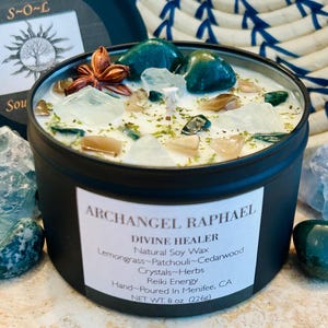 May include: A black candle tin with a white label that reads "Archangel Raphael Divine Healer Natural Soy Wax Lemongrass-Patchouli-Cedarwood Crystals-Herbs Reiki Energy Hand-Poured in Menifee, CA NET WT. 8 oz (226g)". The candle is topped with clear and green crystals, a star anise, and dried herbs.