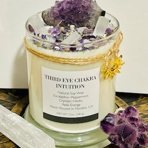 May include: A white candle with a gold sun charm and amethyst crystals. The label reads "Third Eye Chakra Intuition" and lists the ingredients as "Natural Soy Wax, Eucalyptus-Peppermint, Crystals-Herbs, Reiki Energy" and "Hand-Poured in Menifee, CA". The candle is 12 ounces (340 grams).
