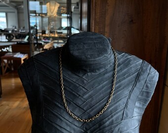 May include: A gold chain necklace on a black mannequin. The chain is a simple, linked design.