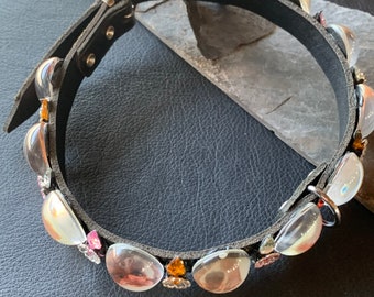 May include: A black leather dog collar with a silver buckle and decorative clear and pink gemstones.