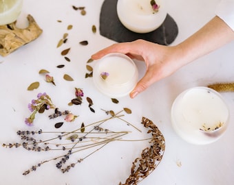 Pode incluir: Três porta-velas de vidro branco com flores secas e ramos de lavanda sobre uma superfície branca.
