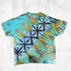May include: A turquoise, yellow, and gray tie-dye t-shirt with a geometric pattern. The short-sleeved shirt has a crew neck and a unique, colorful design. The tie-dye pattern features a repeating starburst motif.