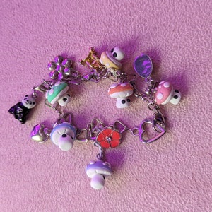 May include: A silver charm bracelet with various charms, including mushrooms, a flower, a heart, and a panda bear. The charms are made of metal and plastic and are painted in various colors.