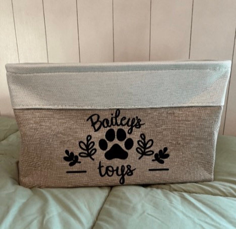 May include: A beige and white storage bin with a black paw print and the text "Bailey's toys" on the front.