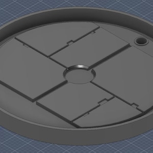 May include: A grey, circular object with a recessed centre and several rectangular sections. The object has a raised outer rim and a small circular hole. The design appears to be a 3D model or a component of a larger structure.