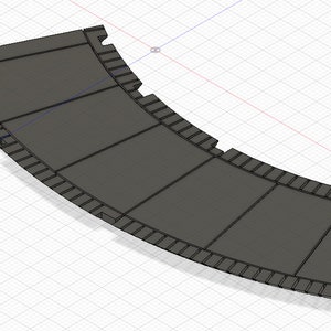 Op de afbeelding: Een gebogen, gesegmenteerd, grijs paneel van plastic of metaal met een reeks kleine, gelijkmatig verdeelde, rechthoekige uitsparingen langs de rand.