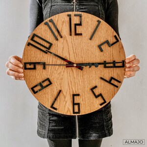 May include: A wooden clock with black numbers and hands. The clock has a light brown wood grain finish.