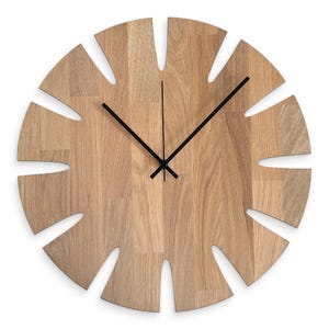 Può includere: Un orologio da parete in legno con un design a forma di foglia. Il quadrante dell'orologio è in legno marrone chiaro con un motivo a venature naturali. Le lancette nere indicano l'ora. L'orologio ha un'estetica unica e moderna.