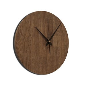 Peut inclure: Une horloge murale ronde en bois avec des aiguilles noires et un centre doré. Le cadran de l'horloge est en bois avec une teinte brun foncé.