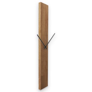 May include: A vertical wooden wall clock with a rectangular shape. The clock is made of light brown wood and has black clock hands. The clock hands are thin and elegant, contrasting with the wood's natural grain. The clock is designed to be mounted on a wall.