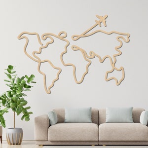Op de afbeelding: Een houten wereldkaart wanddecoratie met een eenvoudig lijndesign. De kaart toont een vliegtuig dat over het continent Azië vliegt. De kaart is gemonteerd op een witte muur boven een lichtbeige bank.