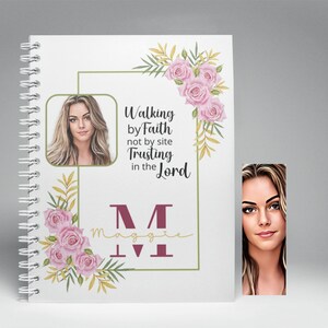 May include: A white spiral bound journal with a floral design and a photo of a woman. The journal has the text "Walking by Faith not by site Trusting in the Lord" and the letter "M" with the name "Maggie" underneath. A bookmark with a photo of a woman is attached to the journal.