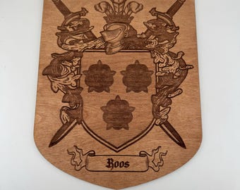 Könnte beinhalten: Hölzernes Familienwappen in Schildform mit Helm, Schwertern und floralen Motiven. Der Name "Boos" wird auf einem Banner unten angezeigt. Das Wappen ist in das Holz geschnitzt.