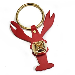 May include: A red lobster-shaped keychain with a gold ring and a gold bell.