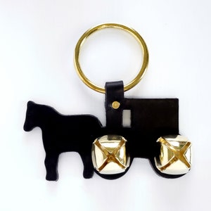 May include: Black leather cutout of a horse-drawn buggy with three gold jingle bells. The buggy is attached to a gold ring.