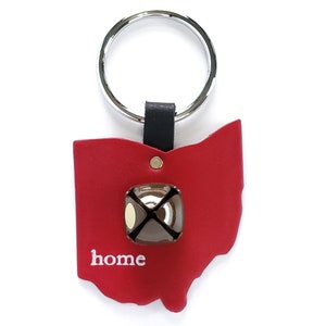 May include: Red leather Ohio state outline keychain with a silver key ring and a small brown bell with the word "home" printed in white.