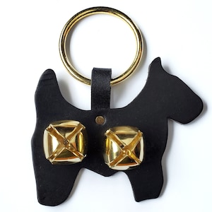 May include: Black leather dog-shaped door knocker with two gold bells. The knocker has a gold ring for hanging.