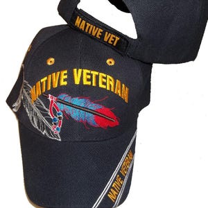 May include: Black baseball cap with gold embroidered text "NATIVE VETERAN" and a feather design. The cap also features the text "NATIVE VET" on the adjustable strap. The design includes red, blue, and silver accents.