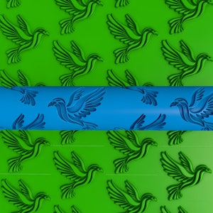 Pode incluir: Um rolo de massa azul com um padrão repetitivo de pássaros estilizados. O rolo está parcialmente enrolado sobre uma superfície verde com o mesmo padrão de pássaros.