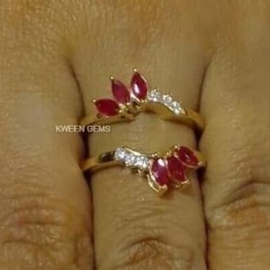 Puede incluir: Dos anillos de oro con un diseño dividido. Los anillos están adornados con piedras de rubí rojo y piedras de circonita cúbica transparentes.
