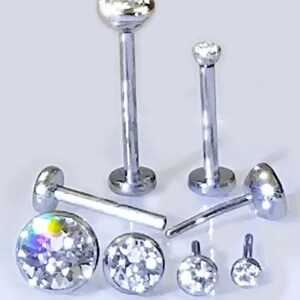 May include: A set of six silver body jewelry pieces with clear crystal accents. The jewelry is made of surgical steel and is suitable for lip, nose, or eyebrow piercings.