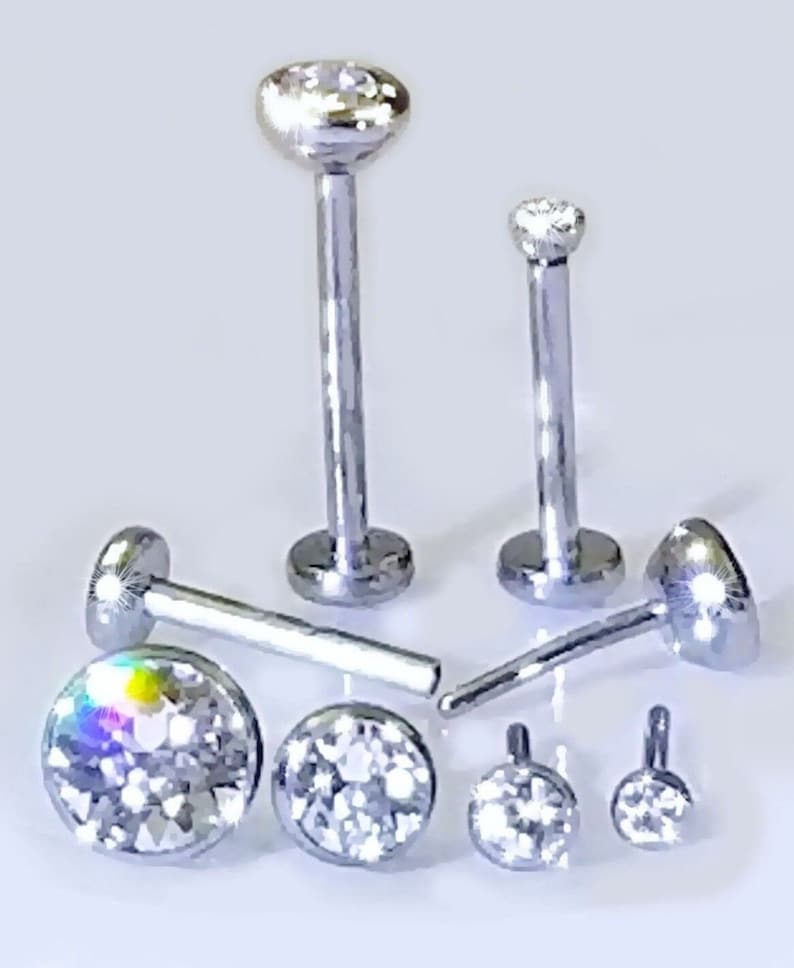 May include: A set of six silver body jewelry pieces with clear crystal accents. The jewelry is made of surgical steel and is suitable for lip, nose, or eyebrow piercings.