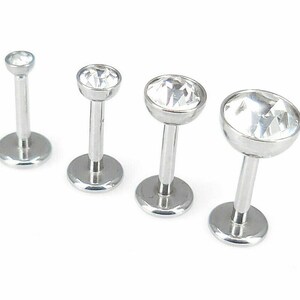 May include: Three silver body jewelry pieces with clear crystal tops. The jewelry is in different sizes.