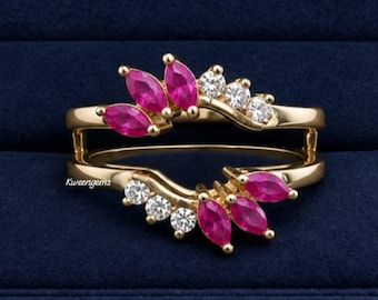 May include: A gold ring guard featuring two curved bands connected at the base. The design includes marquise-cut pink stones and round clear stones arranged in a symmetrical pattern. The text Kweengems is visible on the left side of the ring.