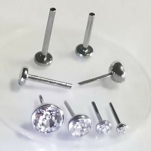 May include: A set of six silver nose rings with clear gem stones. The rings are different sizes and styles.