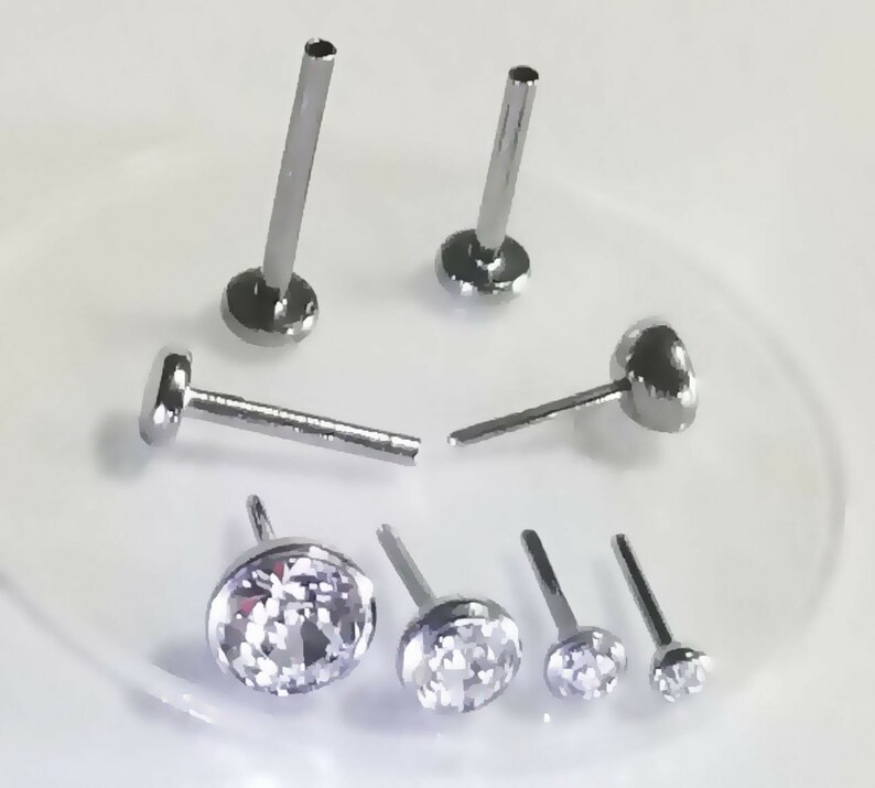 May include: A set of six silver nose rings with clear gem stones. The rings are different sizes and styles.