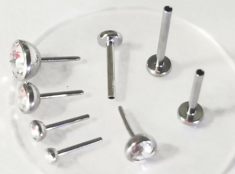 May include: A set of seven silver nose rings with clear crystal accents. The rings are different sizes and styles, including a few with flat backs.