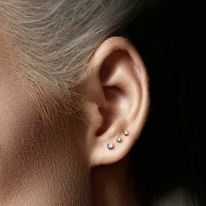 May include: Close-up of a person's ear with three small diamond stud earrings.