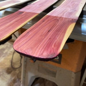 May include: Close-up of wooden paddles with a reddish-purple stain on the paddle blade. The wood grain is visible. The paddles are likely for water sports or decorative use.