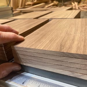 May include: Close-up of several stacks of rectangular wooden planks. The planks are a light brown color with visible wood grain. The edges of the planks are neatly aligned, suggesting precision. The image highlights the texture and natural beauty of the wood.