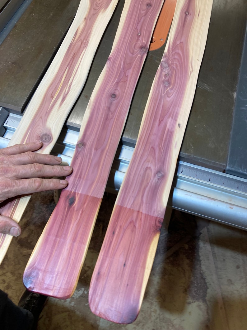 May include: Three unfinished wooden planks with a natural grain pattern. The planks have a light tan outer edge and a vibrant purple-red center. The wood is smooth and appears to be freshly cut, with a slight curve along the edges.