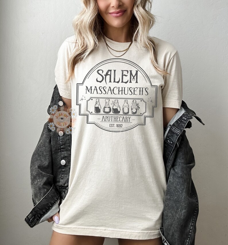 Może przedstawiać: Beżowa koszulka z nadrukiem graficznym vintage'owego szyldu apteki z napisem "Salem, Massachusetts - Apothecary - Est. 1692".
