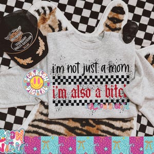 May include: A light gray sweatshirt with the text "I'm not just a mom, I'm also a b*tch" in black and red. A black Harley-Davidson hat and a skull are also visible. The background is a mix of checkered and animal print.