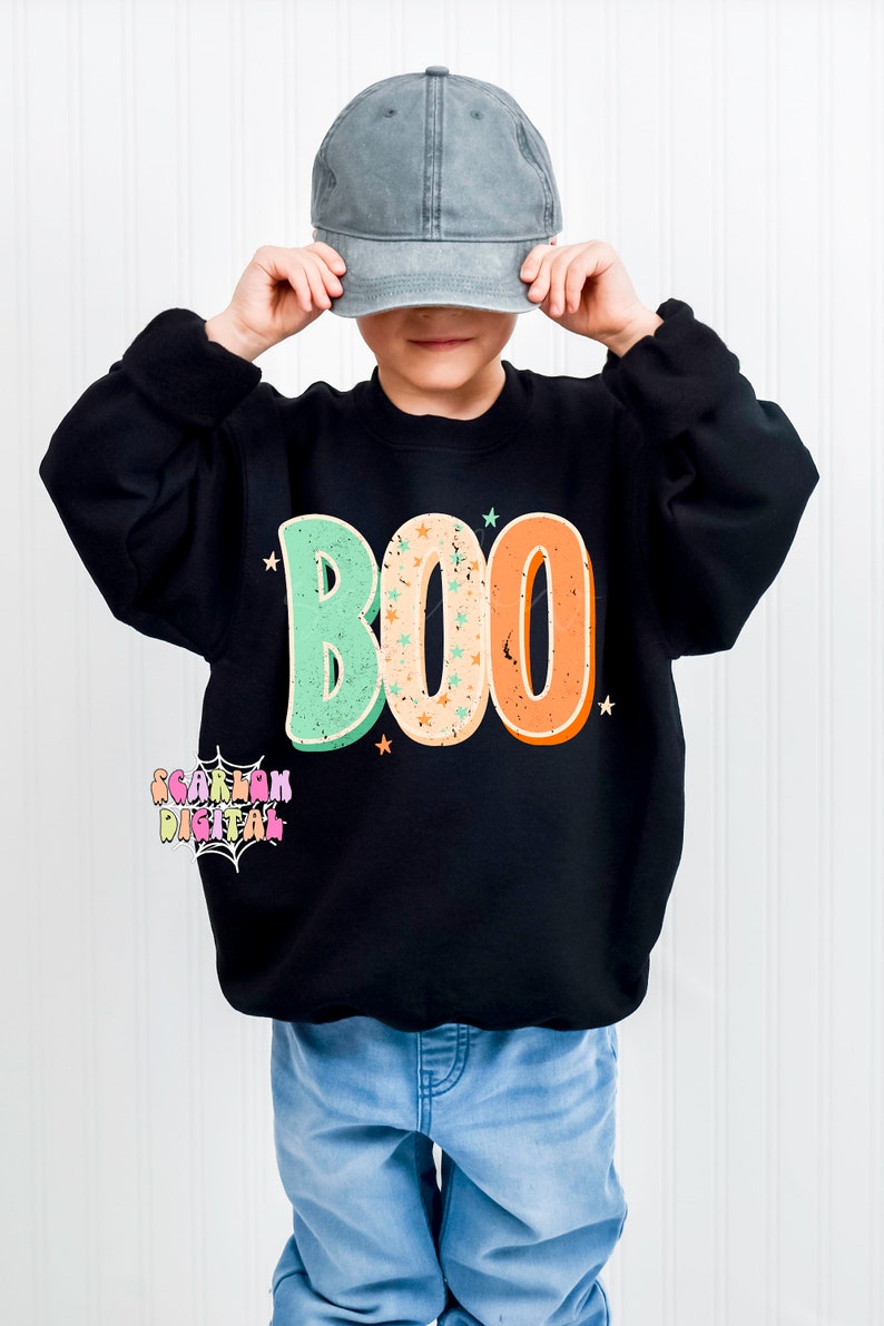 Peut inclure: Un enfant portant un sweat-shirt noir avec le mot "BOO" en lettres r&eacute;tro color&eacute;es et des &eacute;toiles. L'enfant porte une casquette de baseball grise et un jean bleu.