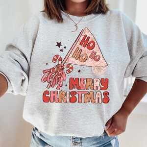May include: A gray sweatshirt with a red and white Christmas graphic. The graphic features a red and white candy cane, a red and white pom-pom, and a red and white banner that says "Ho Ho Ho Merry Christmas".