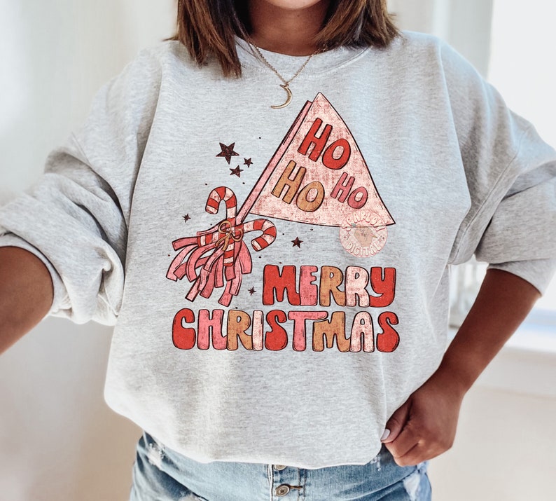 May include: A gray sweatshirt with a red and white Christmas graphic. The graphic features a red and white candy cane, a red and white pom-pom, and a red and white banner that says "Ho Ho Ho Merry Christmas".