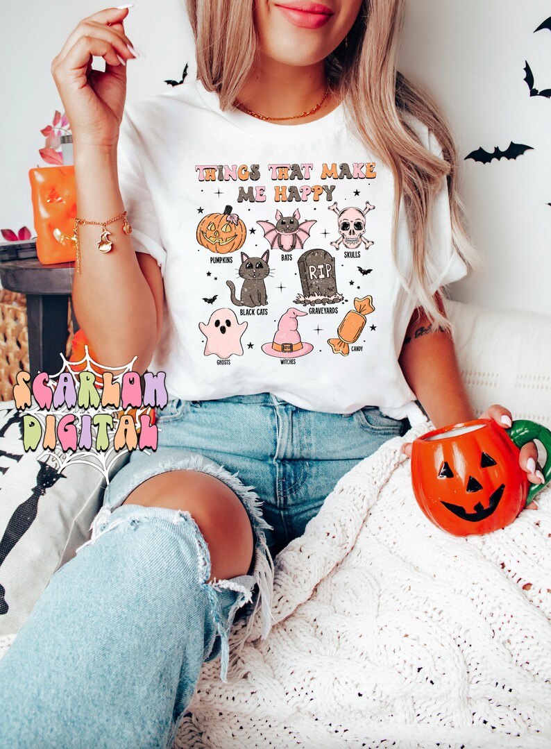 Puede incluir: Camiseta blanca con un dise&ntilde;o gr&aacute;fico de iconos de Halloween y el texto "Things That Make Me Happy". Los iconos incluyen calabazas, murci&eacute;lagos, calaveras, gatos negros, fantasmas, brujas, cementerios y caramelos.