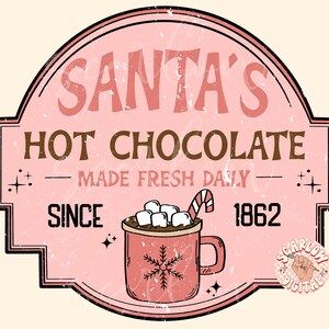Op de afbeelding: Een roze en bruin vintage-stijl bord met de tekst "Santa's Hot Chocolate - Made Fresh Daily - Since 1862". Naast de tekst is een rode mok met marshmallows en een snoepstok afgebeeld.